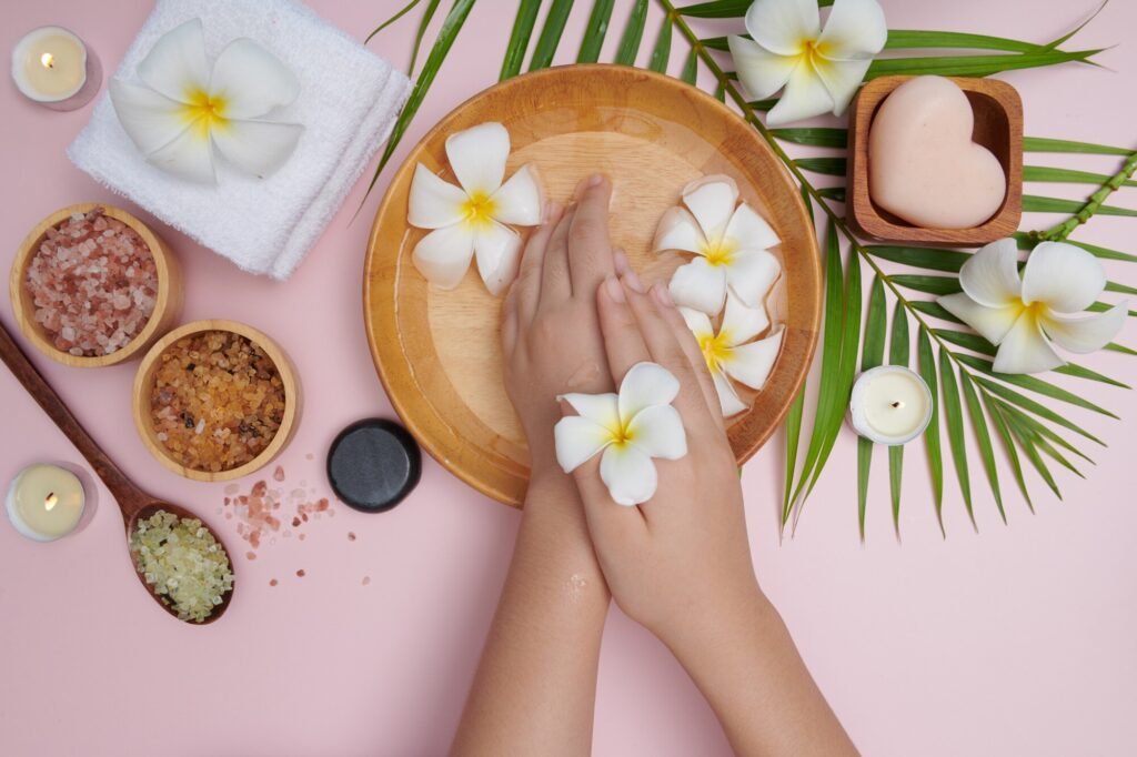 About Us woman soaking her hands bowl water flowers spa treatment product female feet hand spa massage pebble perfumed flowers water candles relaxation flat lay top view 1150 44579